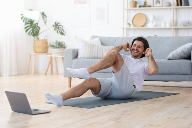 Positive guy making exercises at home, looking at laptop screen